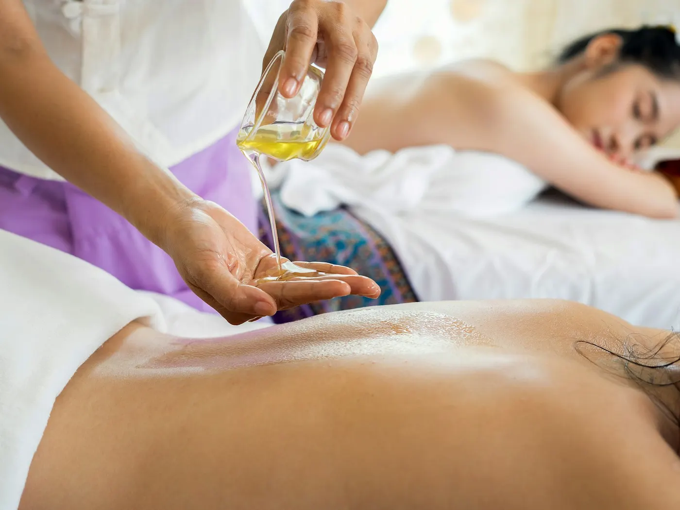 Therapist pouring aromatherapy oil onto a client's back before a massage