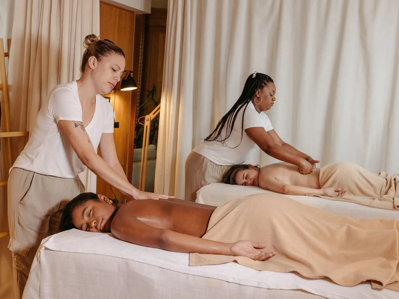 Two clients receiving a massage side by side from two therapists